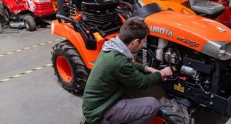 Apprenti mécanicien avec les mains dans le moteur d'un petit tracteur
