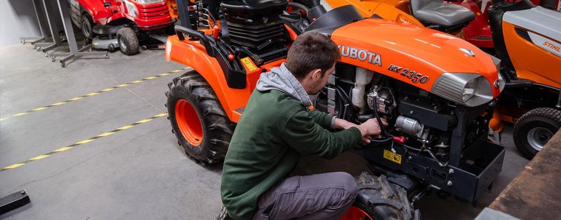 Apprenti mécanicien avec les mains dans le moteur d'un petit tracteur