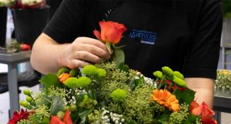 Jeune apprentie fleuriste apporte la touche finale à la conception d'un bouquet en ajoutant une rose orange